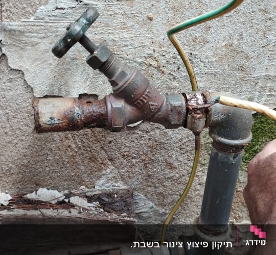 יד מחזיקה צינור ליד ברז חלוד על קיר